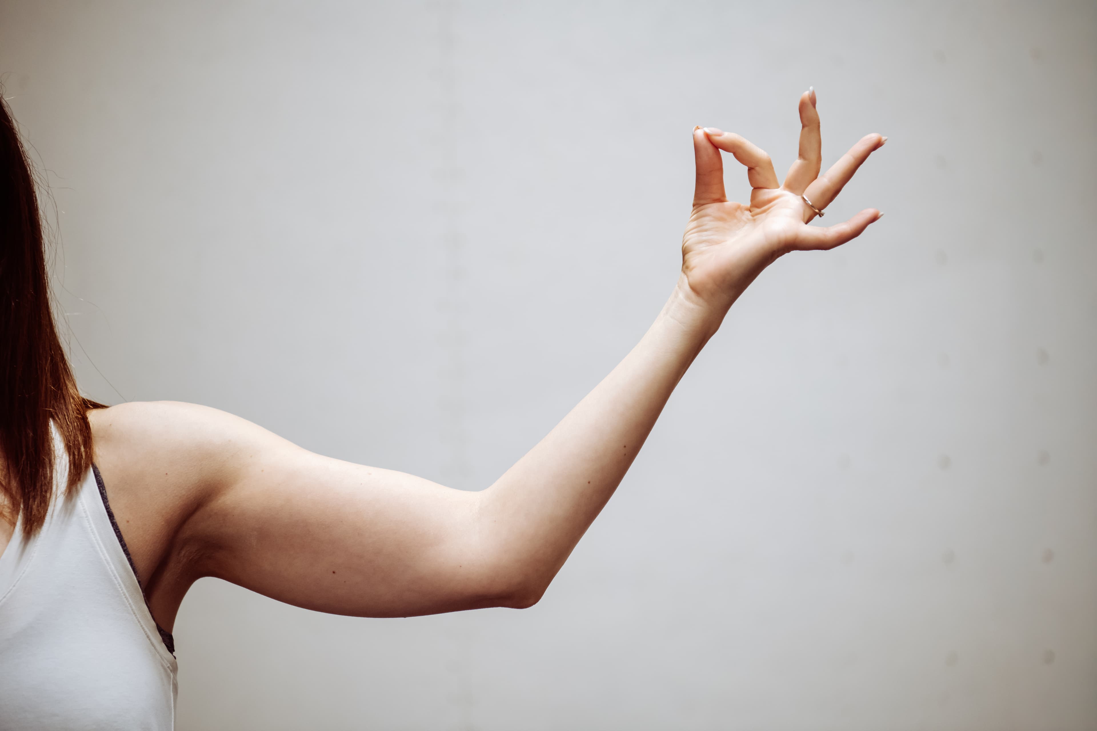 Weiblicher Arm mit einer Yoga-Mudra-Handgeste, Daumen und Zeigefinger berühren sich vor hellem Hintergrund.